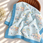 A light blue quilted baby blanket with a cute cartoon bear pattern and a solid blue border, draped over a brown wicker basket with dried flowers on a sunlit white surface.