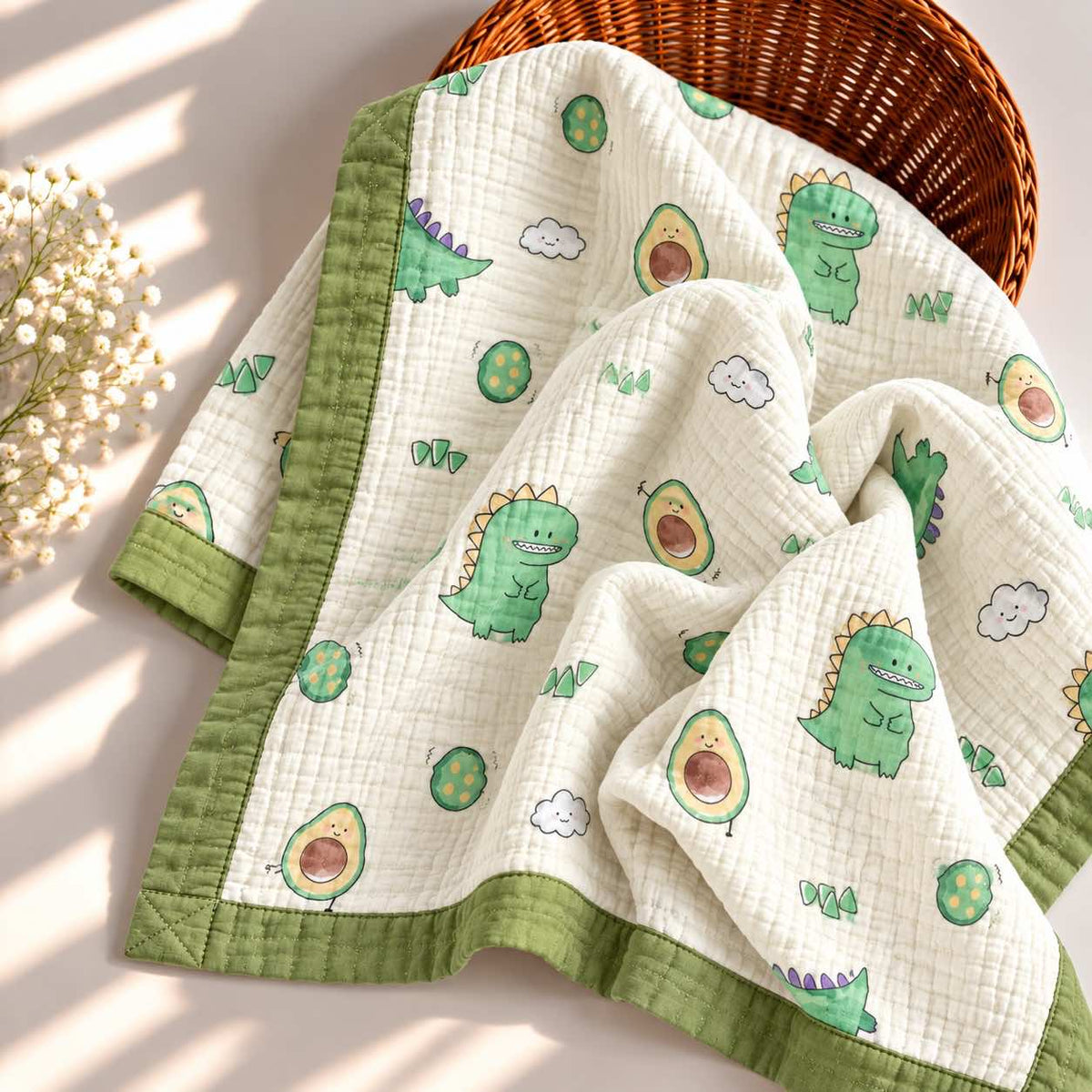 A quilted baby blanket with a green dinosaur and avocado print, draped over a woven basket on a sunlit surface.